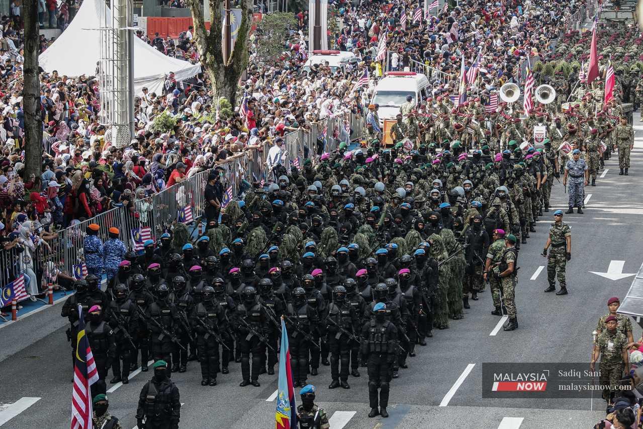 Malaysian Armed Forces personnel stand in formation as the crowds press against the dividers. 
