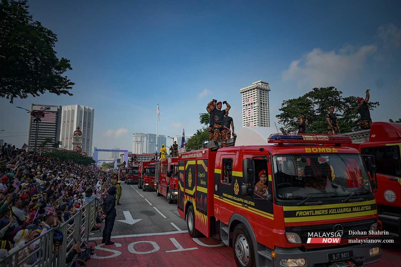 Firemen show off their muscles as the fire engines roll by. 
