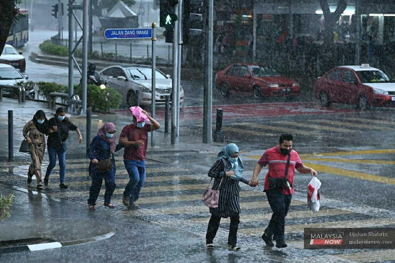 Pedestrians shield themselves from the rain as they run across the road in Jalan Dang Wangi, Kuala Lumpur. 
