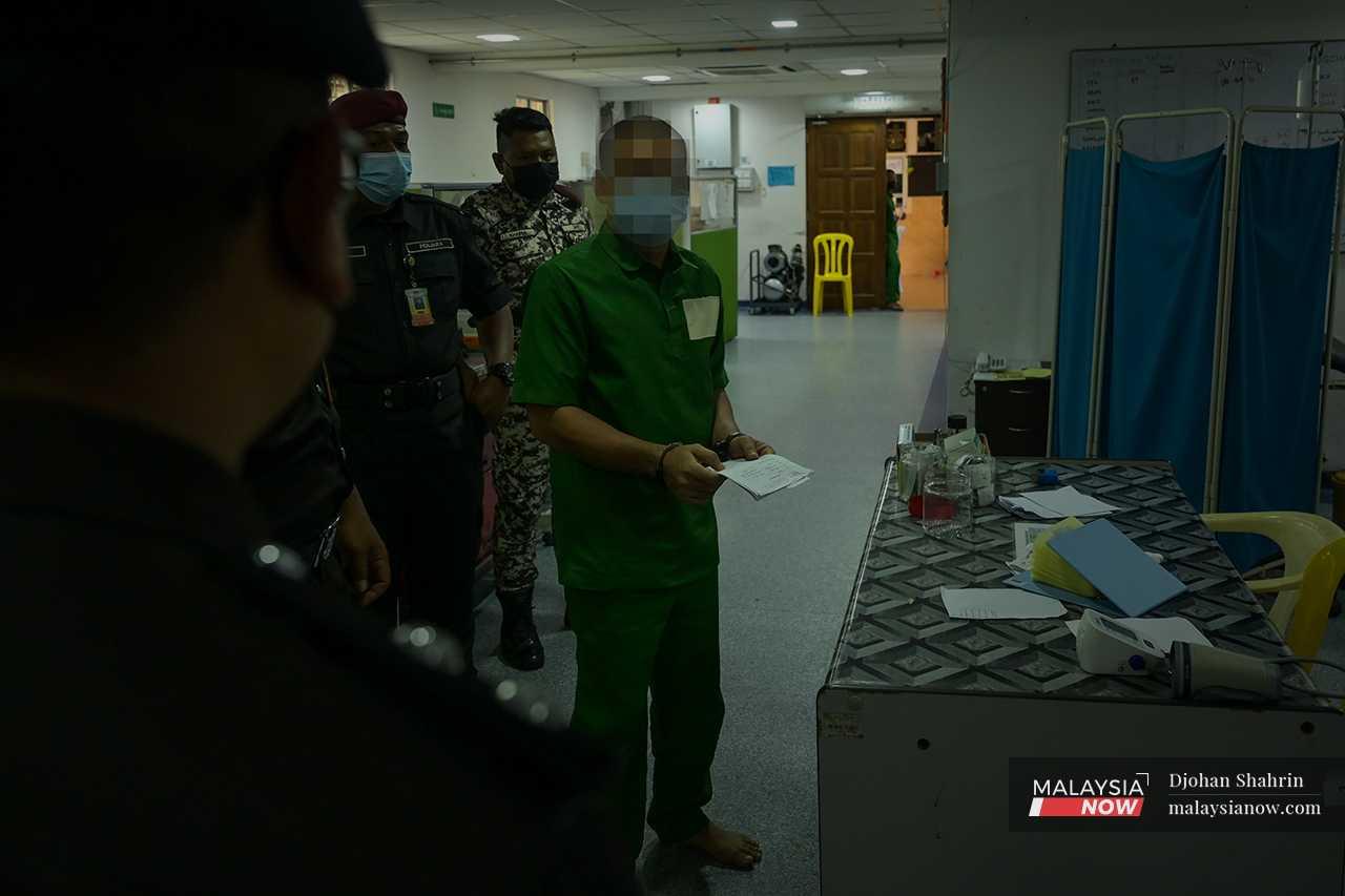 A prisoner holds his medical records under the watchful eye of the prison wardens. 