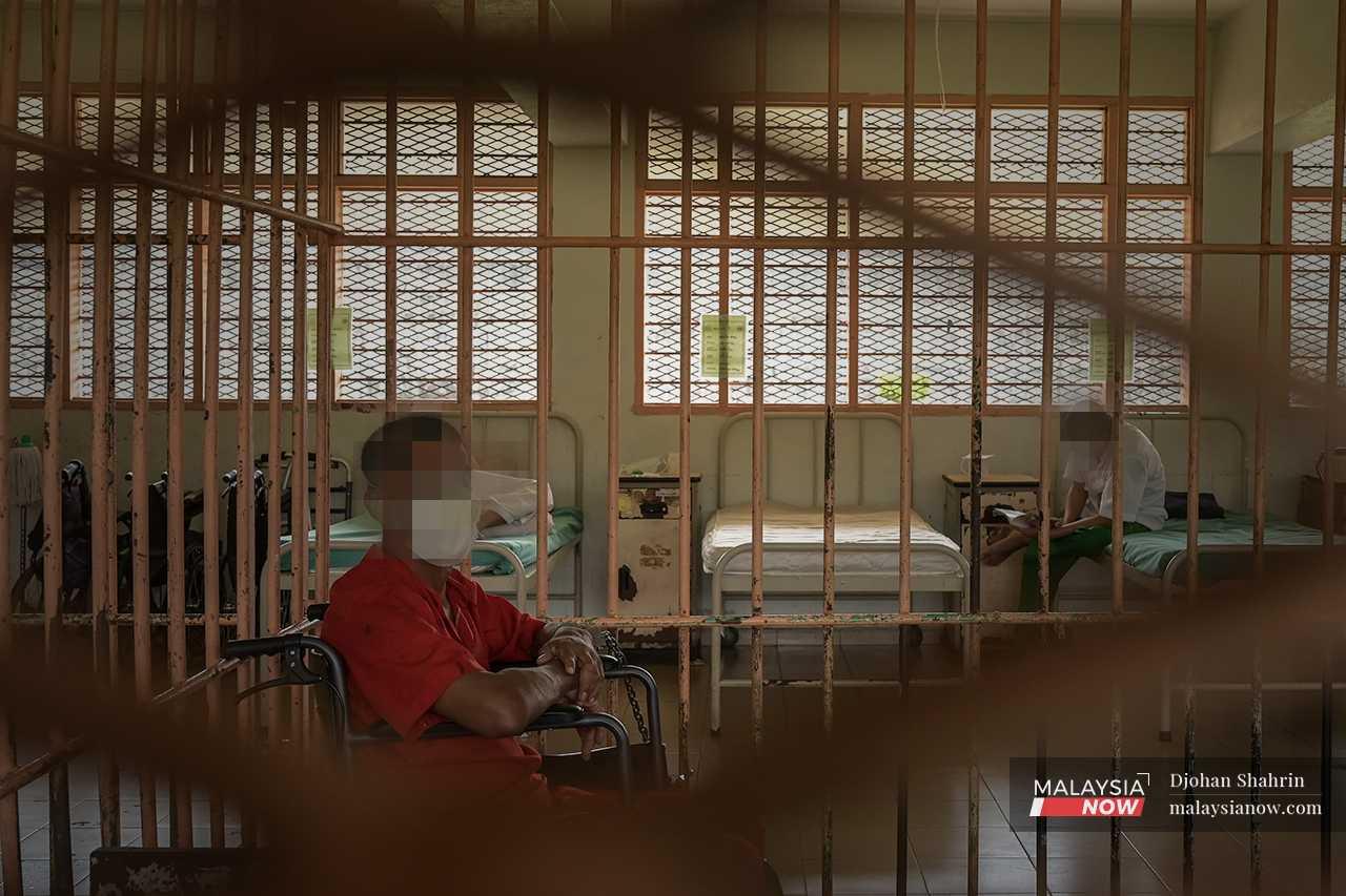 A prisoner still under observation sits handcuffed in a separate section of the ward kept for those who exhibit aggressive behaviour towards the other inmates. 
