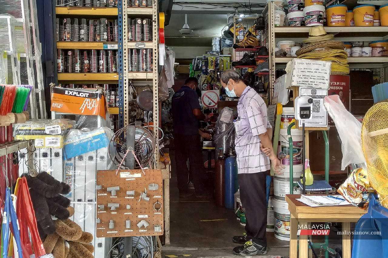 Seorang pelanggan menunggu di luar kedai barang peralatan dan perkakasan di Shah Alam, Selangor.