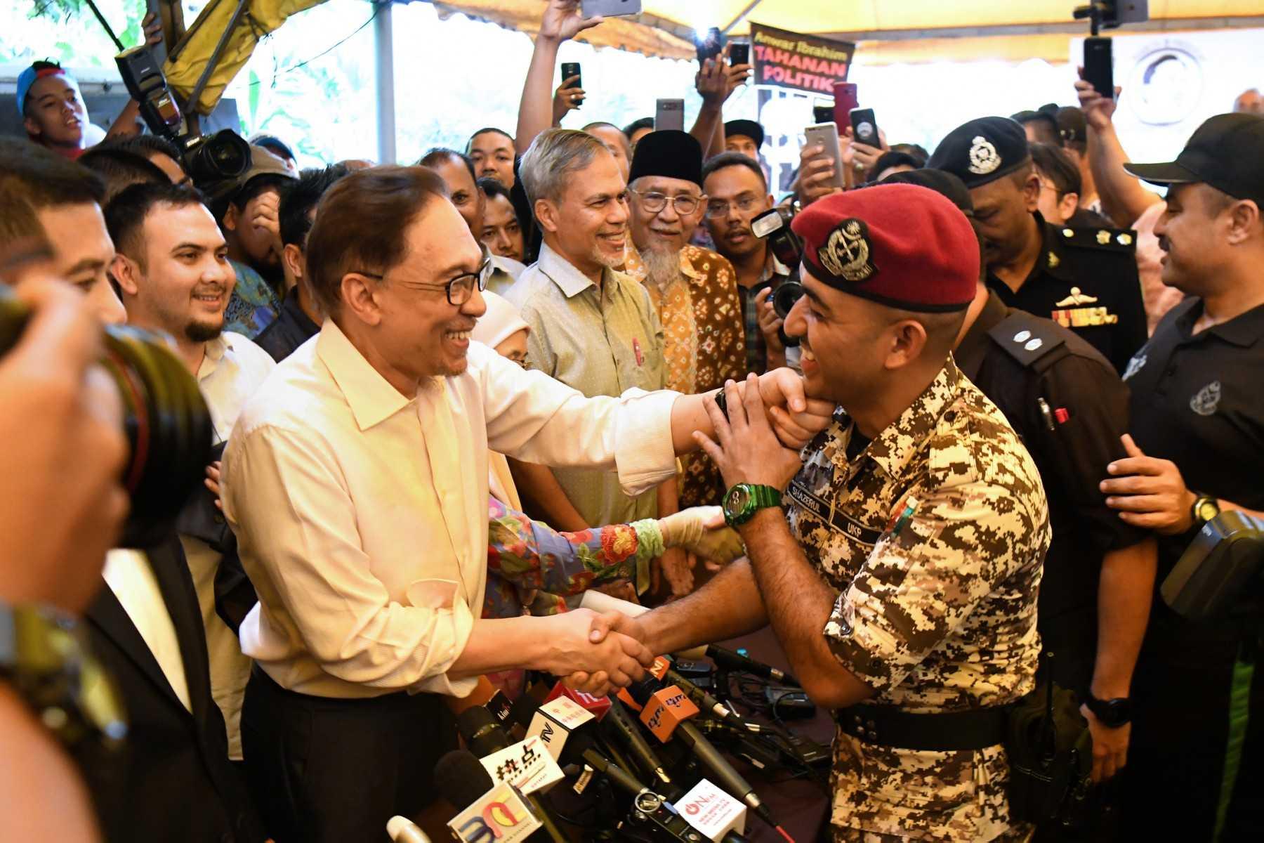 Opposition leader Anwar Ibrahim (left) shakes hands with a prison officer as he speaks to the media after his return home following his release from the Cheras Rehabilitation Hospital in Kuala Lumpur on May 16, 2018. Photo: AFP
