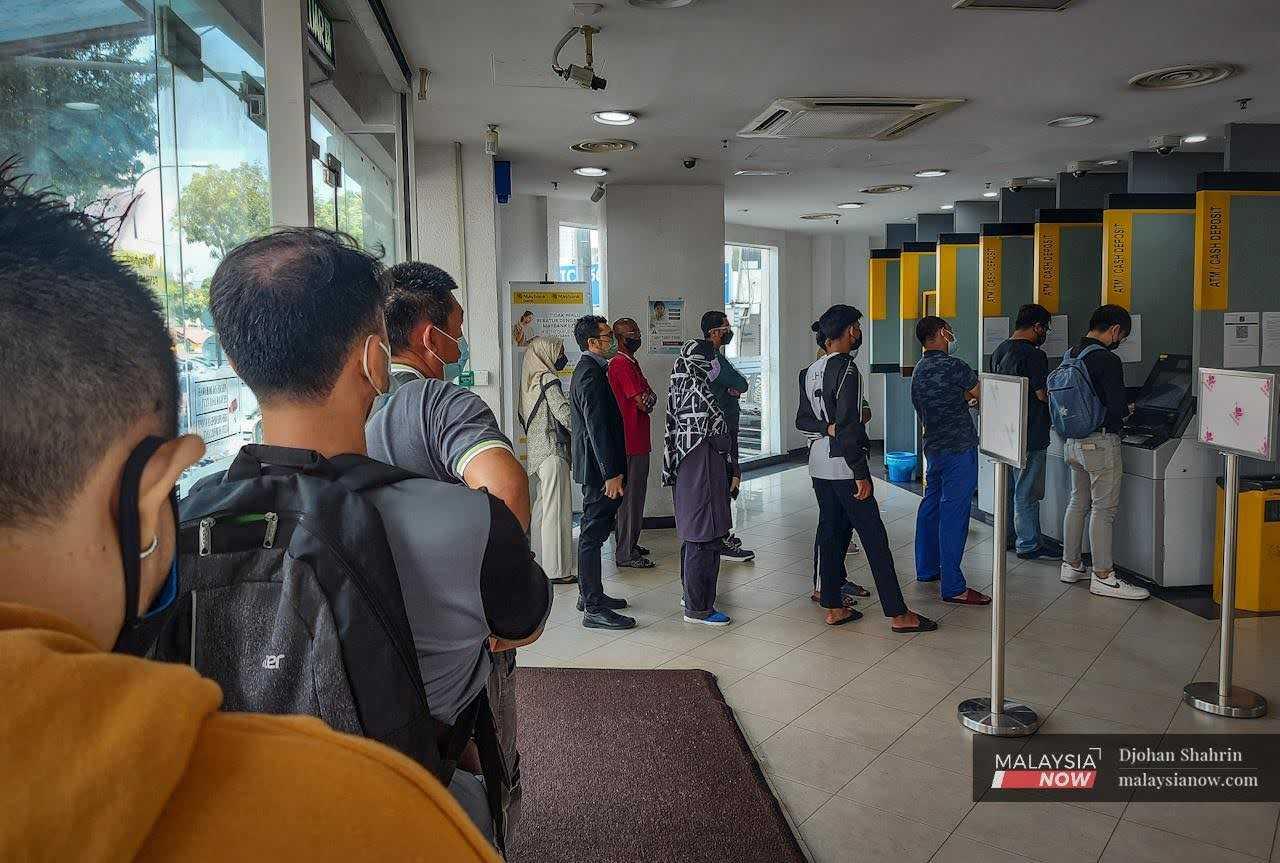 Orang ramai beratur menunggu giliran untuk mengeluarkan wang tunai dari mesin ATM.