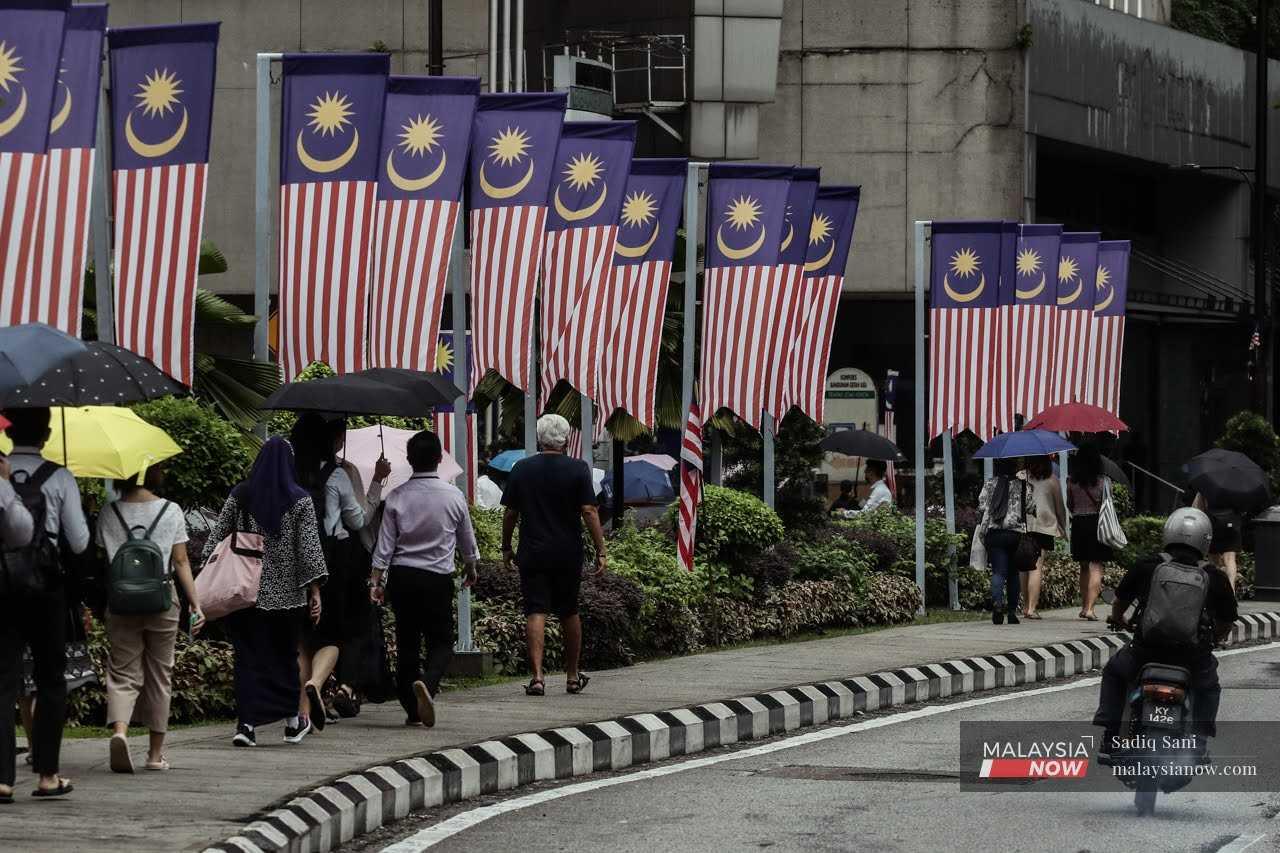 Pedestrians walk along Jalan Ampang in Kuala Lumpur as Malaysian flags flutter overhead. 