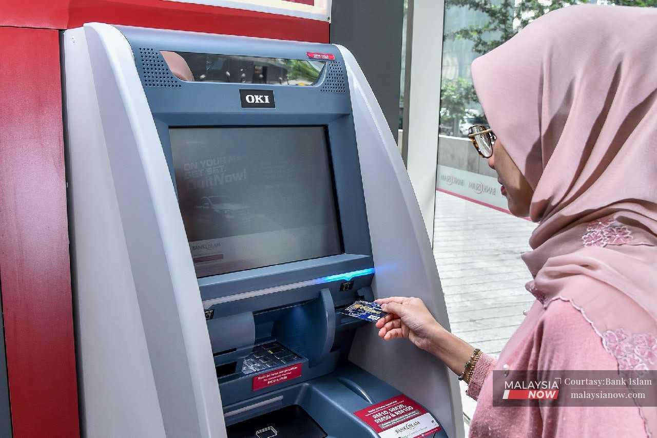 Seorang wanita sedang menggunakan mesim ATM untuk mengeluarkan not kertas ringgit di pusat bandar Kuala Lumpur.