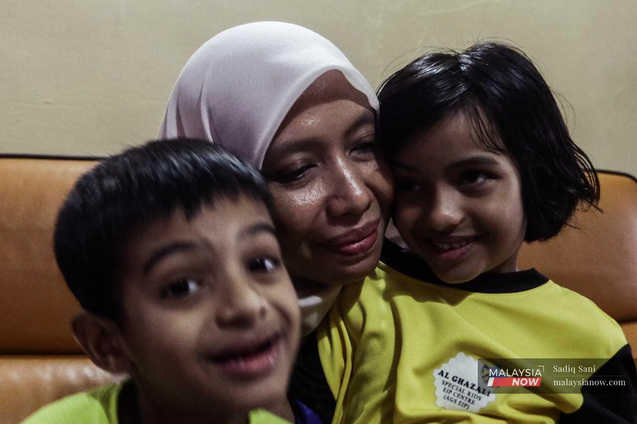 Aini holds her children Rayyan and Hana close. Both of them have been diagnosed with autism, and require special care.