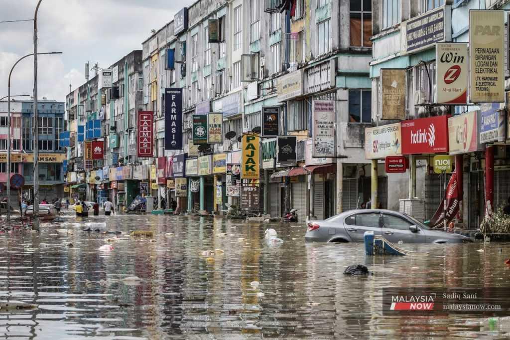 Garbage floats on the water around a partially submerged car as people wade through nearly waist-high floodwaters at a commercial area in Taman Sri Muda, Shah Alam, during the floods which hit Selangor last December. 