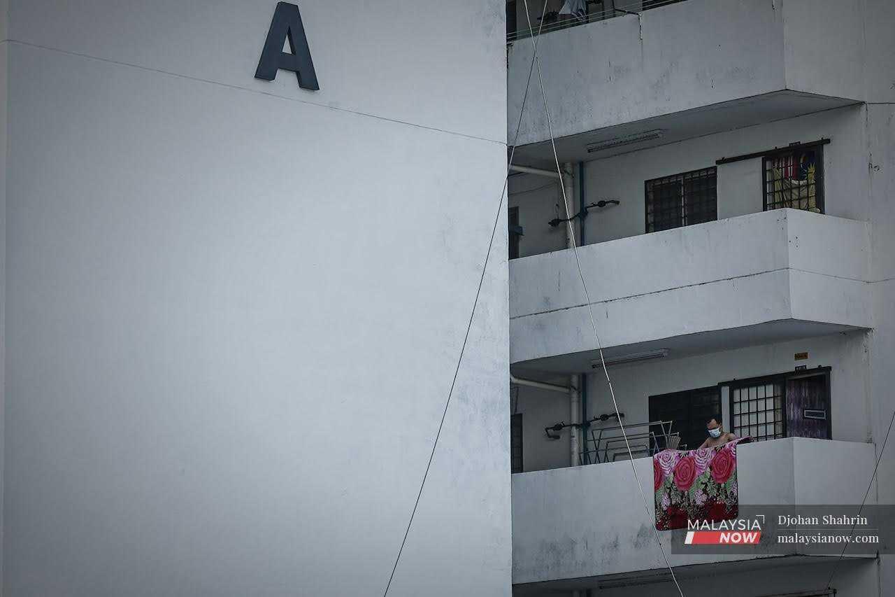 Seorang lelaki menjemur tikar rumahnya di balkoni koridor di hadapav unit rumah di flat kos rendah di Kuala Lumpur.