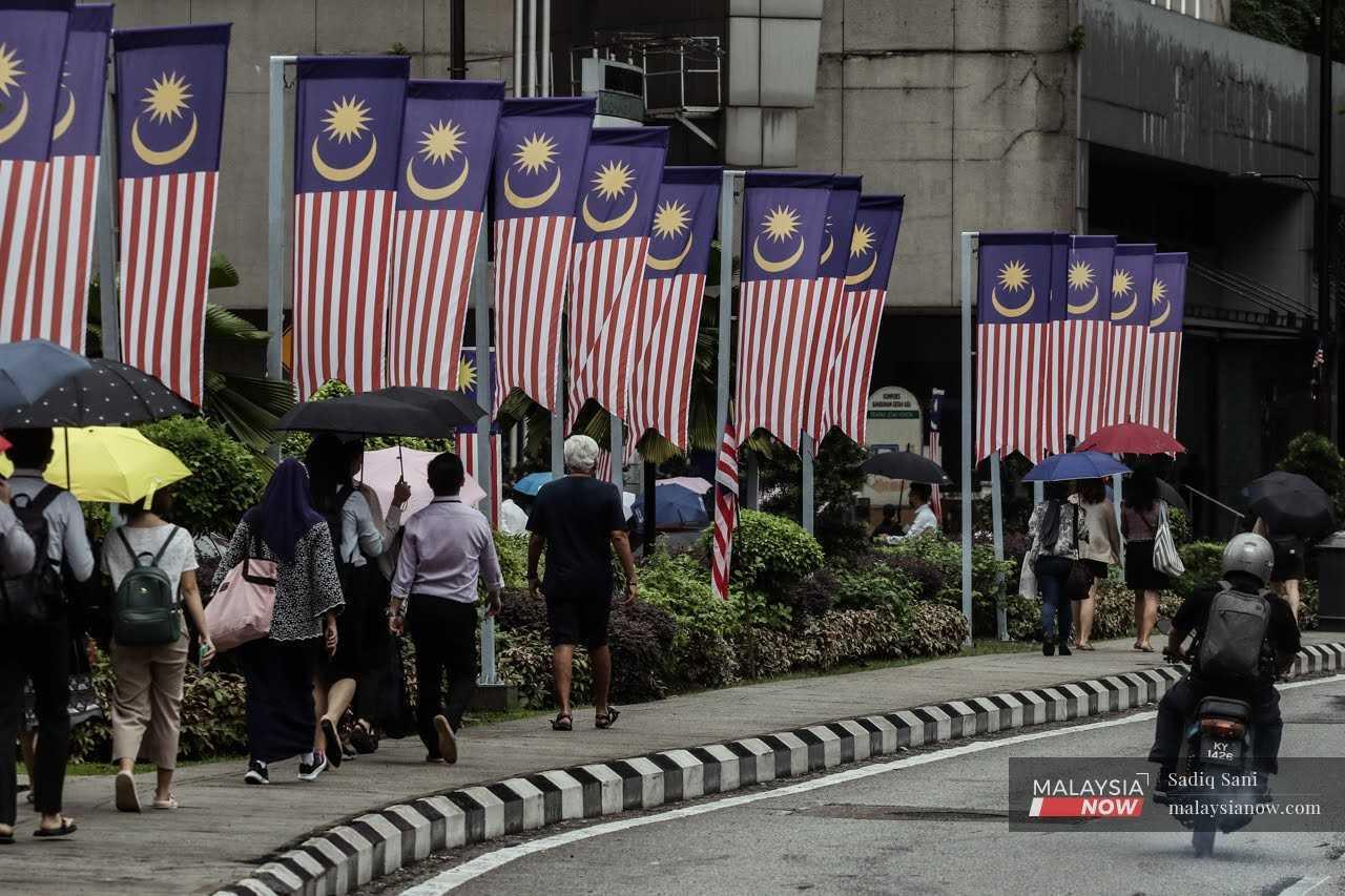 Pedestrians walk along Jalan Ampang in Kuala Lumpur as Malaysian flags flutter overhead.