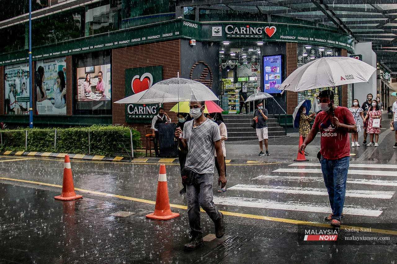 Pedestrians shield themselves from the rain with umbrellas as they cross a street in Bukit Bintang, Kuala Lumpur.