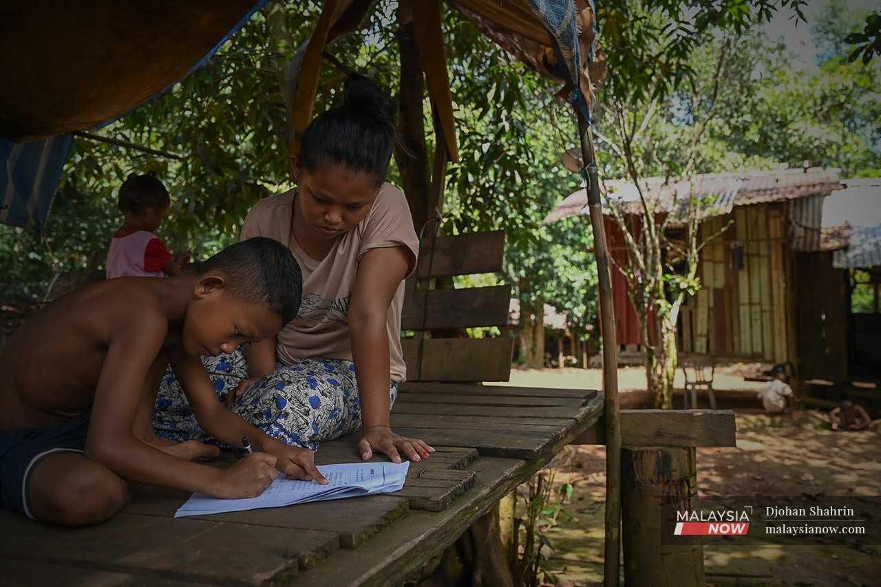 An Orang Asli woman helps her child with his homework at their village in Tasik Chini, Pahang.
