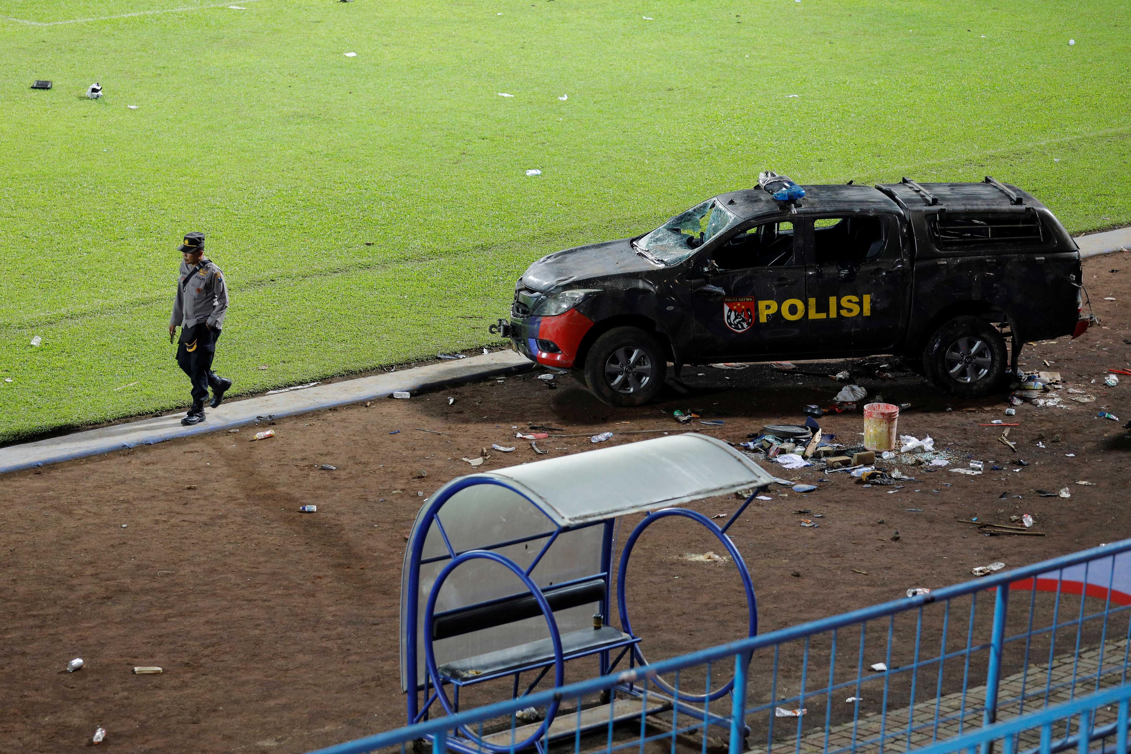 Pegawai polis berjalan di tepi kenderaan polis yang rosak akibat rusuhan di padang Stadium Kanjuruhan, Malang selepas perlawanan antara Arema FC dan Persebaya Surabaya pada 2 Oktober lalu. Gambar: Reuters 