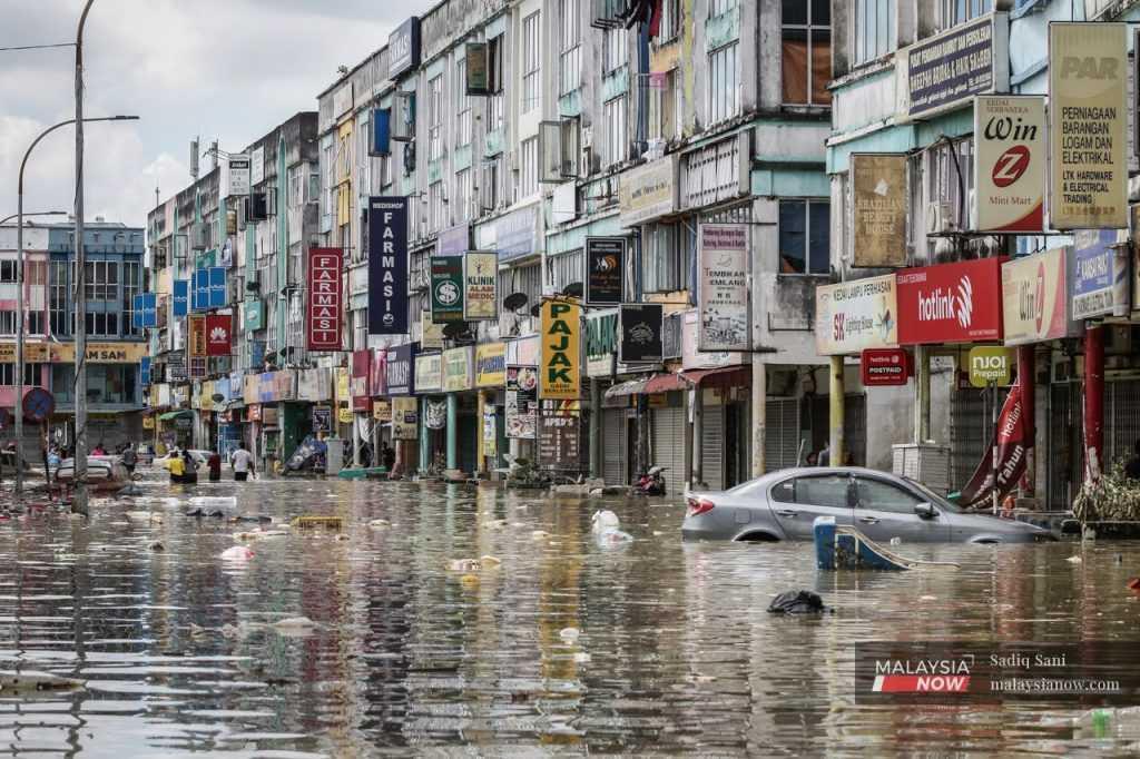 Garbage floats on the water around a partially submerged car as people wade through nearly waist-high floodwaters at a commercial area in Taman Sri Muda, Shah Alam, during the floods which hit Selangor last December.