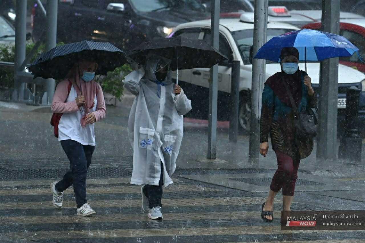 Pedestrians shield themselves from the rain with umbrellas as they cross the road at Jalan Dang Wangi in Kuala Lumpur in this November 2020 file photo. 
