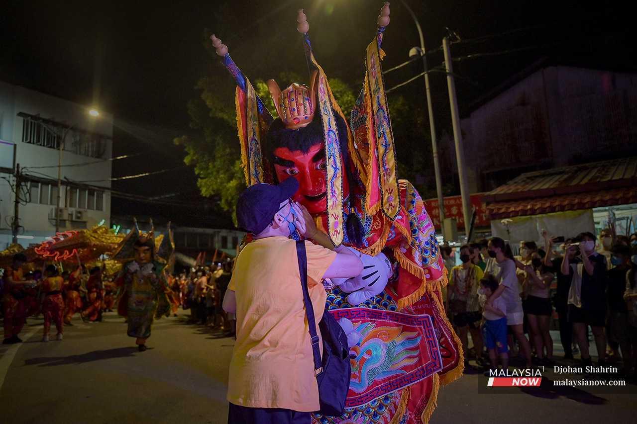 A man whispers something to a performer dressed up as one of the gods during the Nine Emperor Gods procession. 
