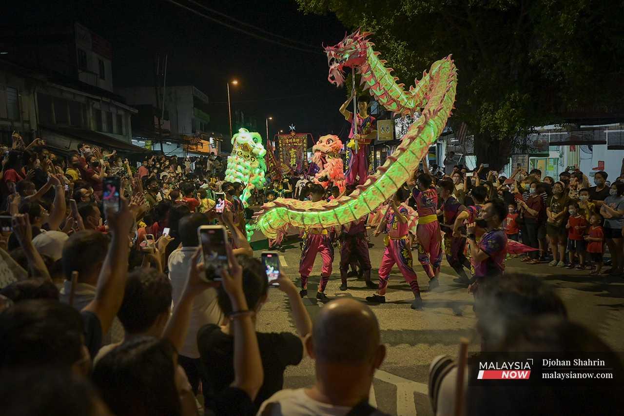 Crowds gather to watch a dragon dance, taking pictures of the colourful performance. 