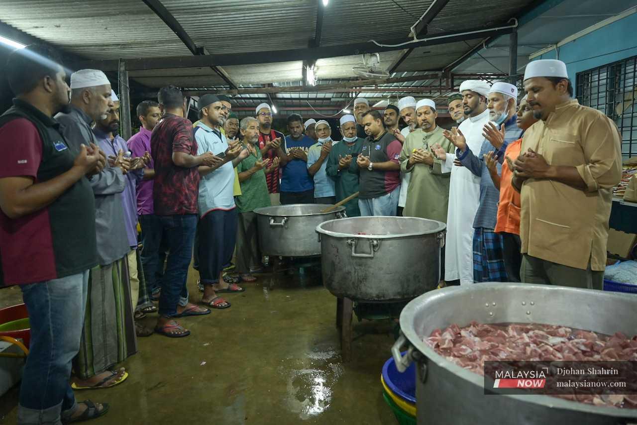 The imam (fourth from left) leads those present in a prayer before the cooking process begins.