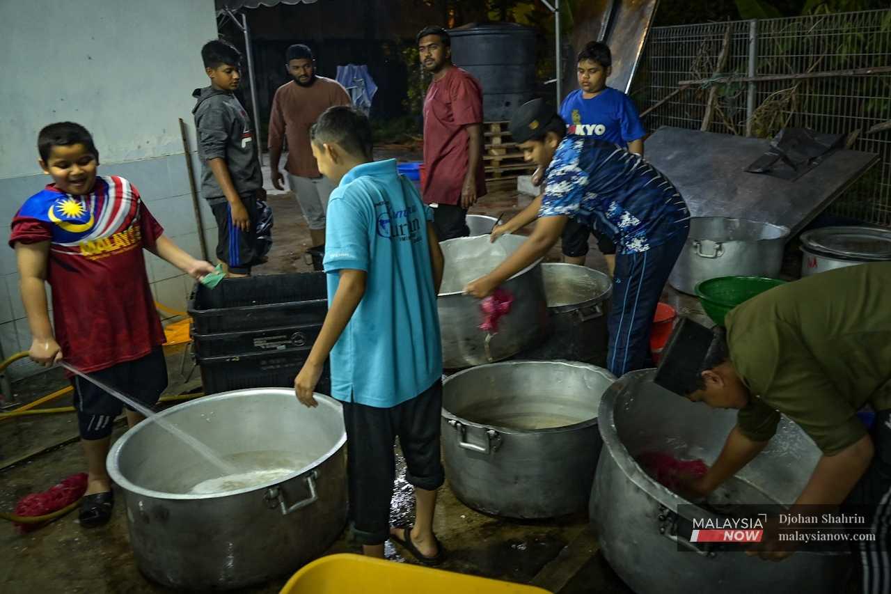 Children help to wash out large pots a day before the Maulidur Rasul event, where thousands of meals are distributed to participants and the surrounding residents.