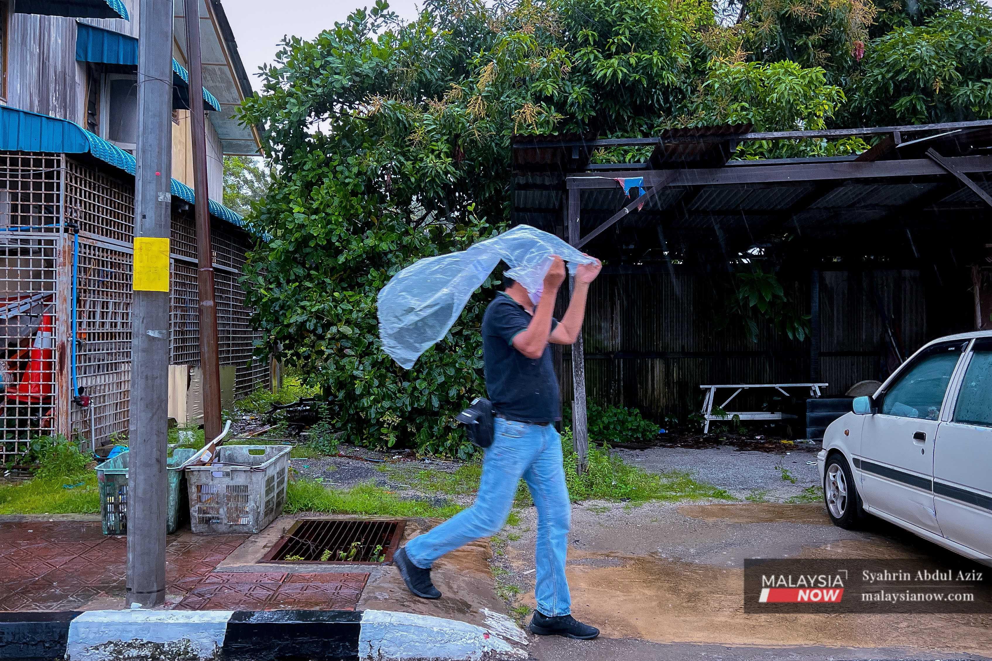 Seorang lelaki menggunakan plastik untuk melindungi diri daripada hujan lebat di Kuala Lumpur.