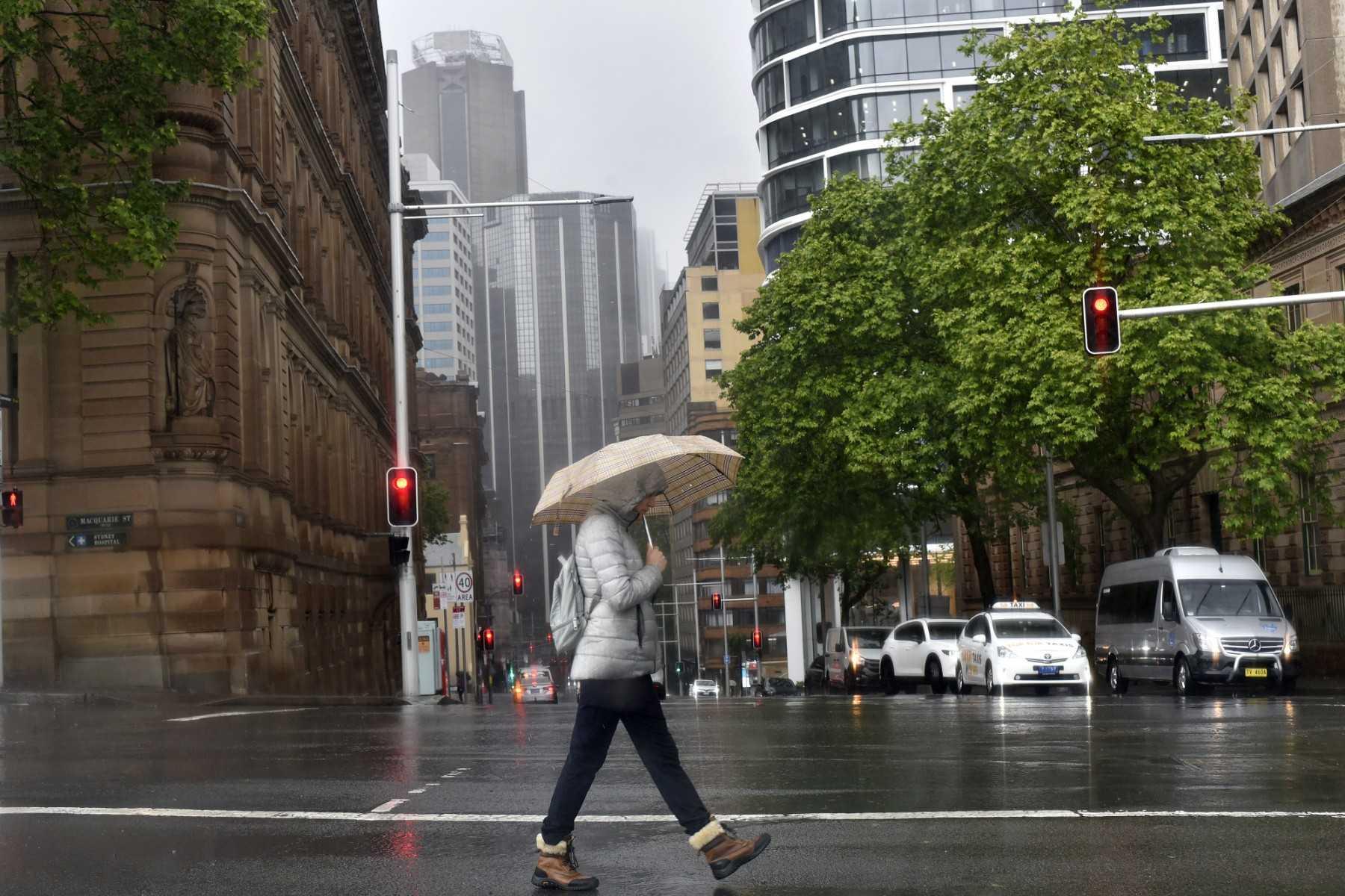 A woman shelters from the rain under an umbrella while crossing a street in Sydney on Oct 6. Photo: AFP