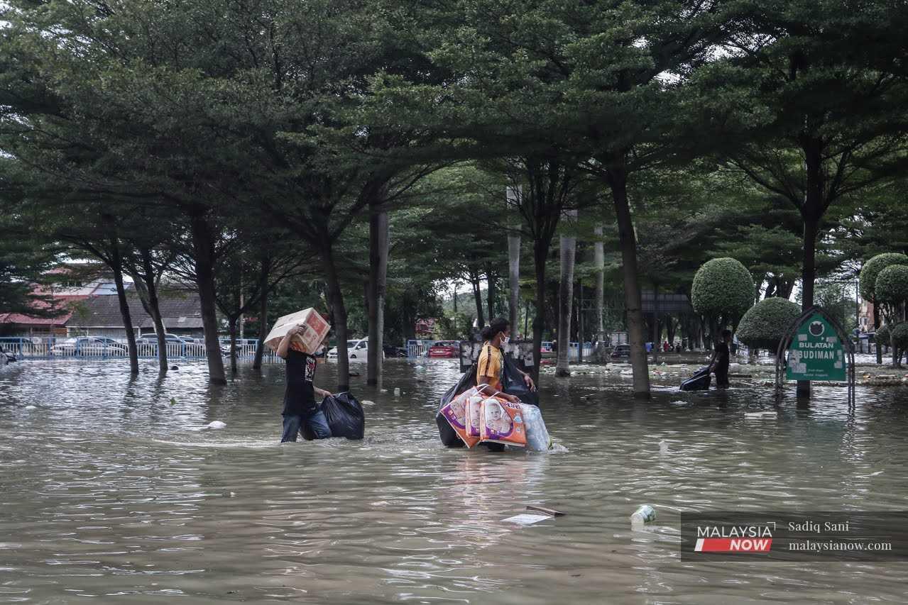 Dua orang penduduk membawa barangan keperluan di sambil meredah banjir ketika bencana banjir di Sri Muda, Shah Alam tahun lalu.
