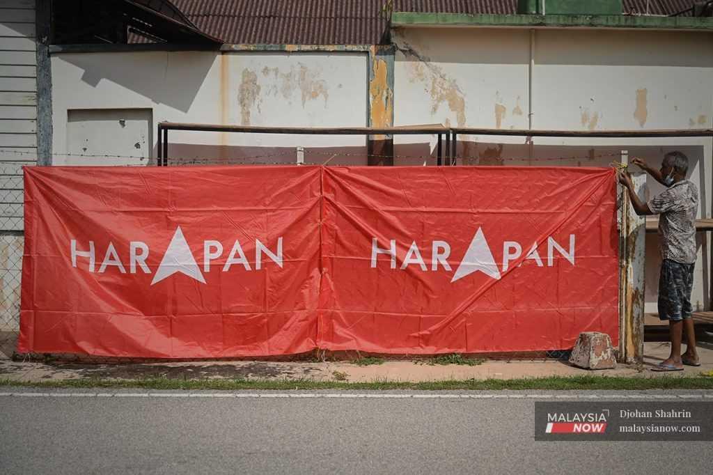 A man hangs banners showing Pakatan Harapan's logo along a fence in the Portuguese Settlement in Melaka ahead of the state election there last November.