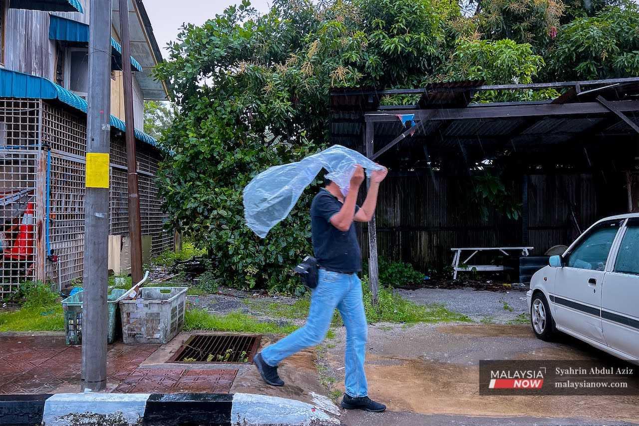 A man uses a plastic sheet to shield himself from the rain in this file picture.