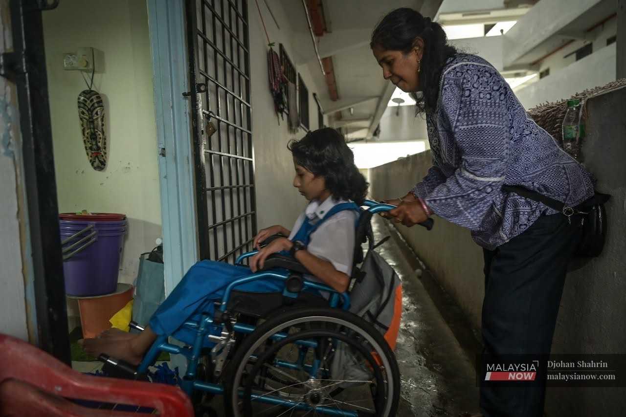 M Kalaichelvi menolak anaknya yang berkerusi roda masuk ke dalam rumah mereka di flat PPR Kerinchi, Pantai Dalam, Kuala Lumpur.