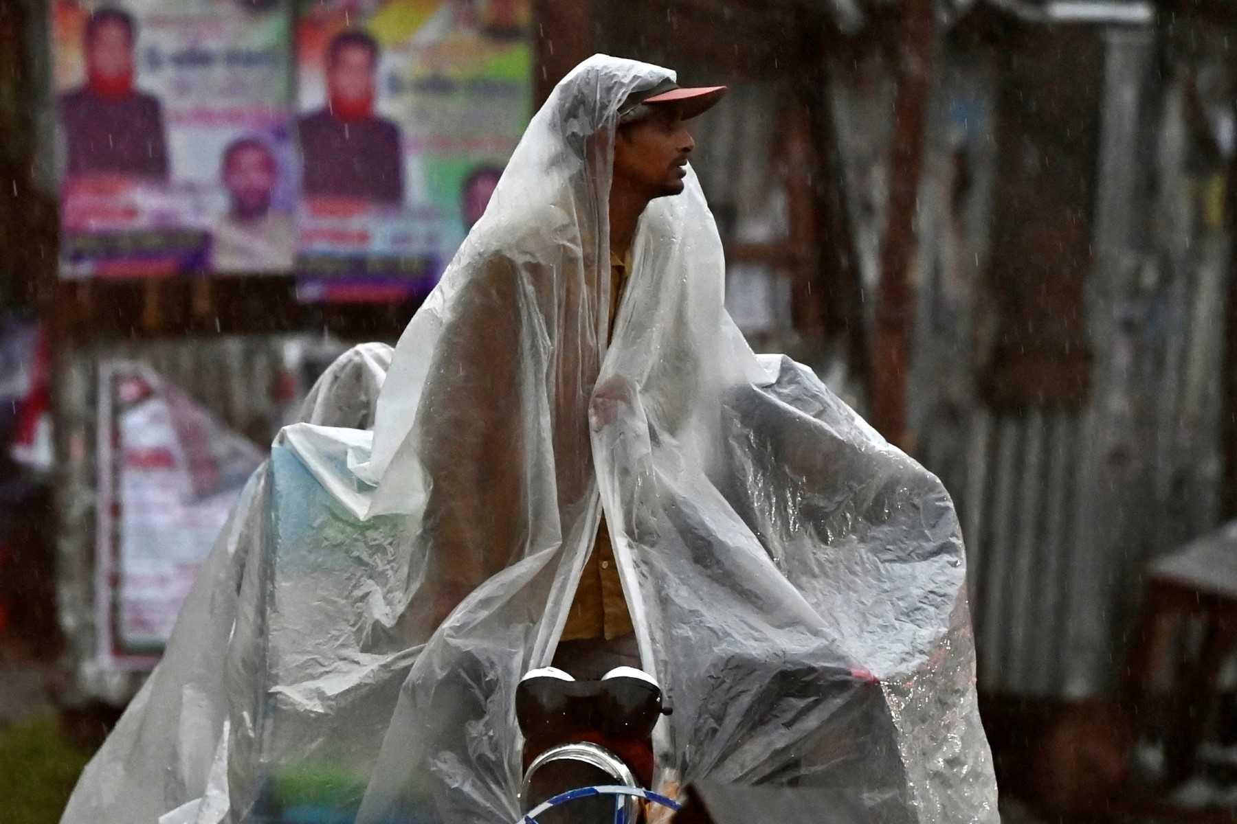 A rickshaw driver uses a plastic sheet to protect himself from rain while waiting for passengers along a street in Faridpur on Oct 24. Photo: AFP