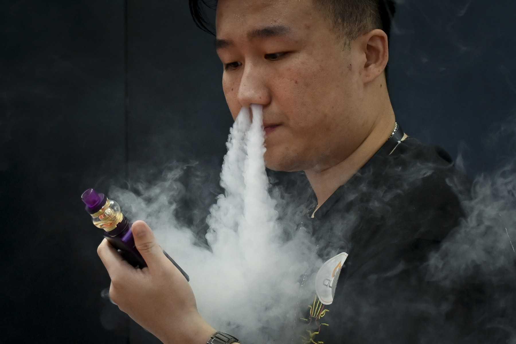 A promoter of an e-cigarette company smokes an electronic cigarette at the Beijing International Consumer Electronics Expo on June 28, 2019. Photo: AFP