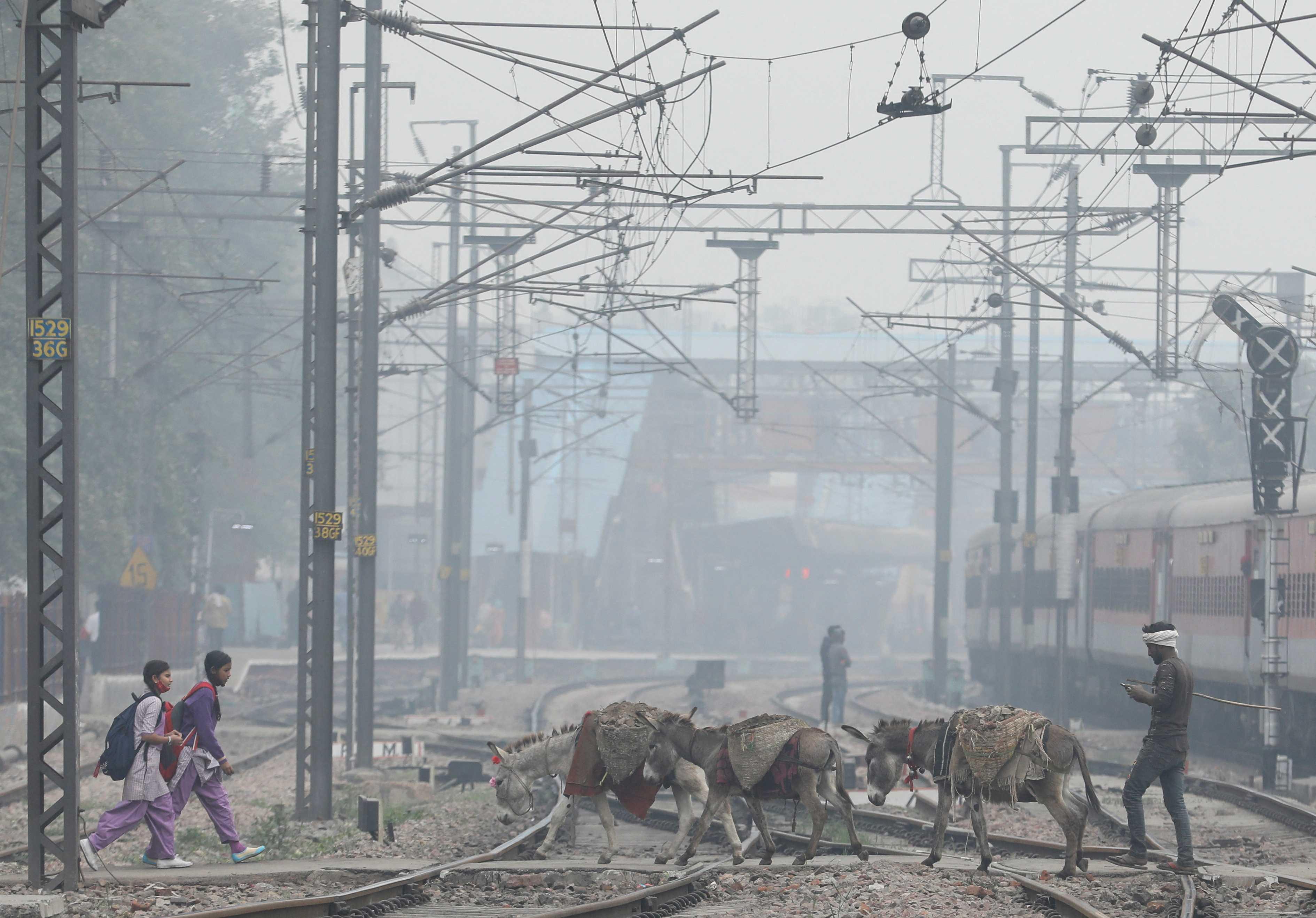 School girls and mules are seen crossing railway tracks on a smoggy morning in New Delhi, India, Dec 2, 2021. Photo: Reuters