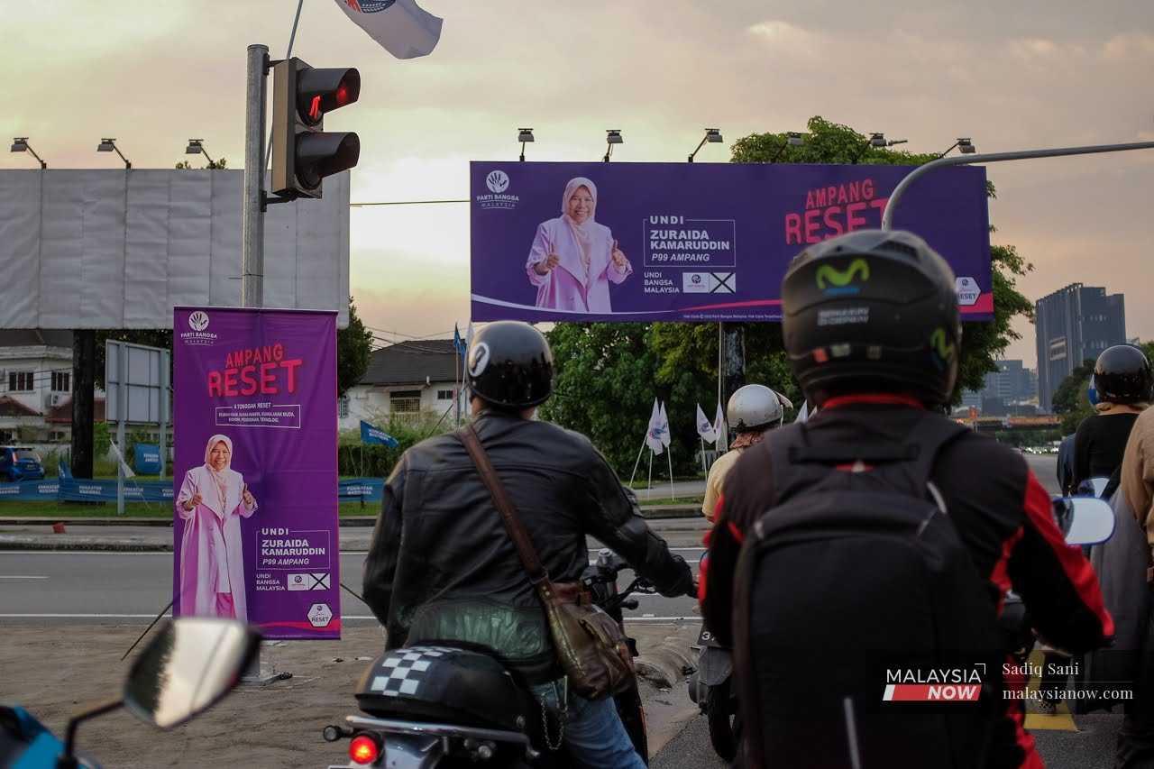 Motorcyclists wait at a junction in Ampang, near a banner and billboard featuring Ampang incumbent Zuraida Kamaruddin.
