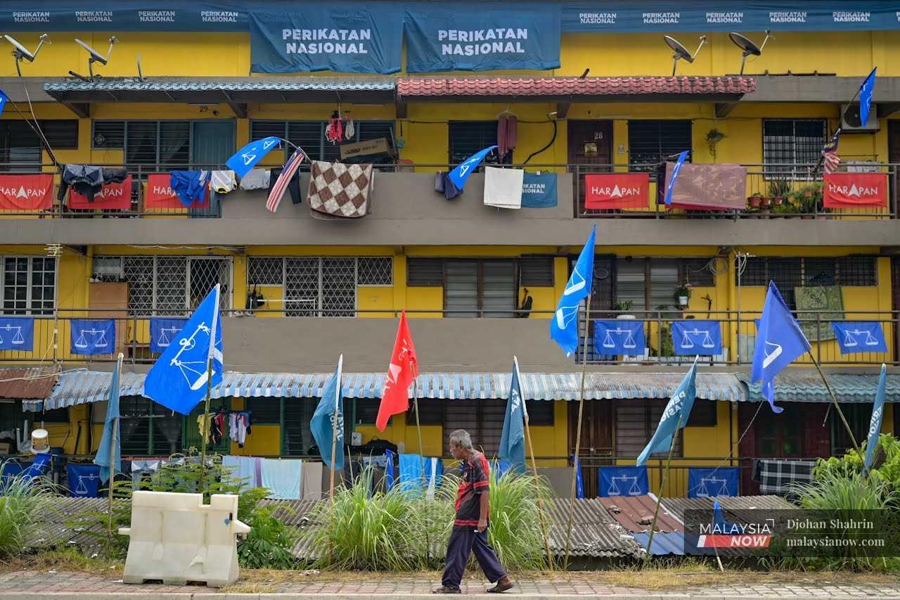 Seorang warga emas berjalan di hadapan flat pangsapuri yang dimeriahkan dengan warna-warni bendera parti.

