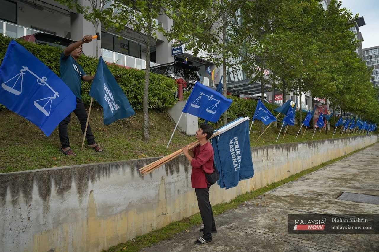Sukarelawan Perikatan Nasional menancapkan bendera di sepanjang pembahagi jalan raya di Taman Tasik Permaisuri.