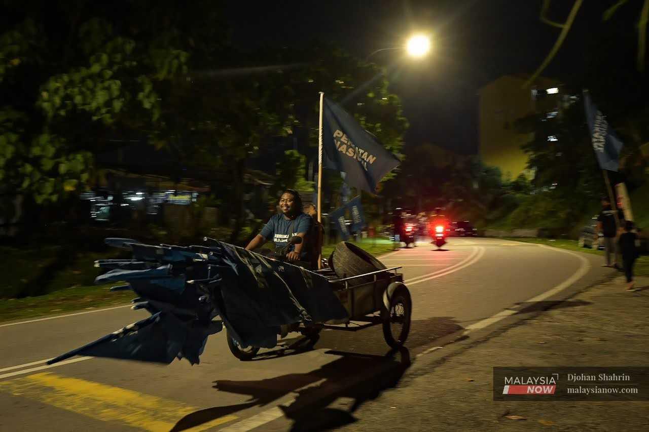 Kerja pemasangan bendera dibuat sehingga larut malam, namun sukarelawan tetap ceria membawa bahan kempen menggunakan motorsikal beroda tiga.