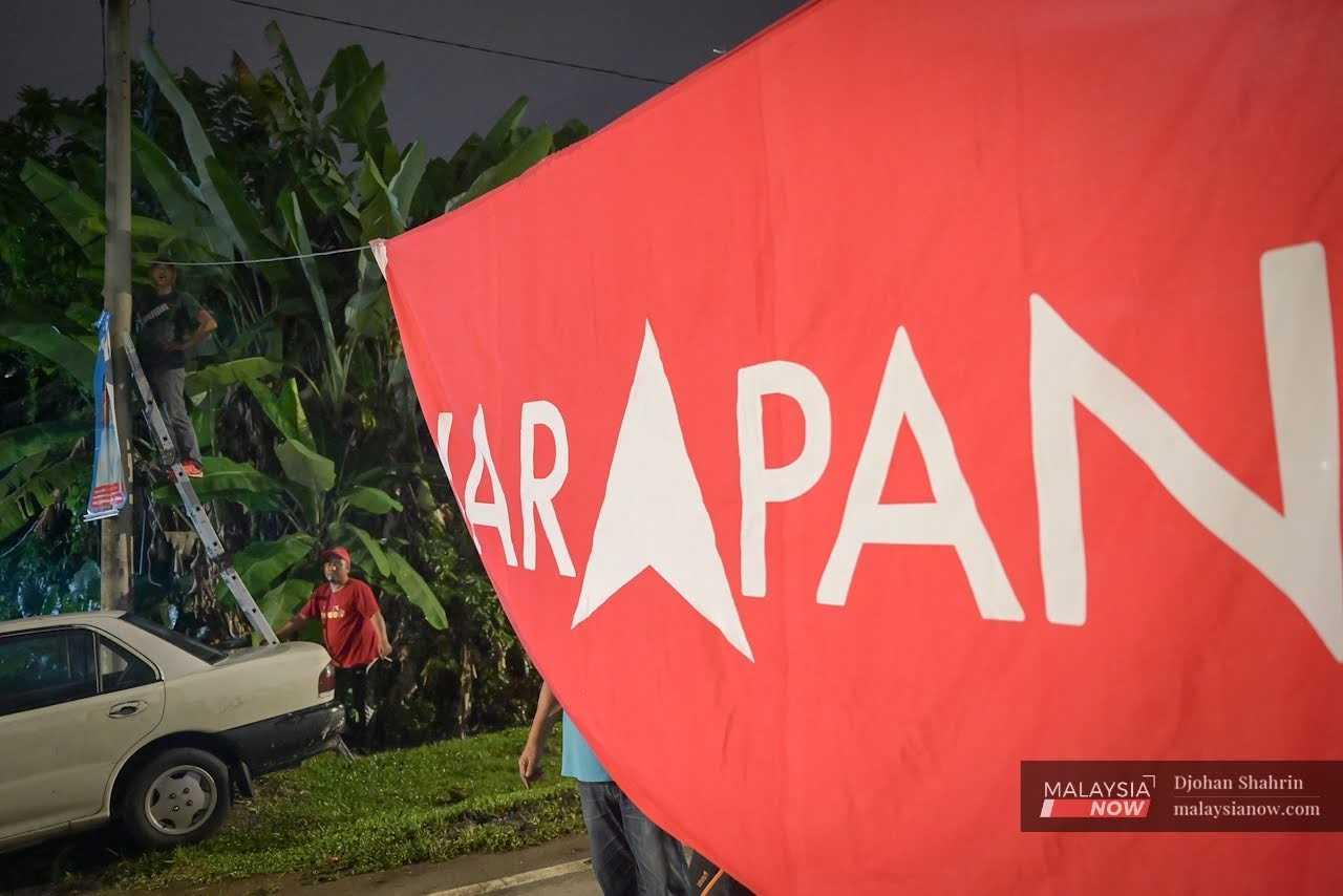 Party workers use a ladder to reach the necessary height to fasten a giant Pakatan Harapan banner across the road. 