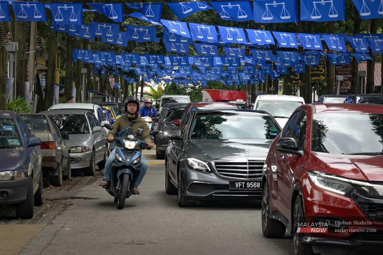 A motorcyclist weaves through traffic beneath strings of flags in Jalan Raja Alang, Kampung Baru.