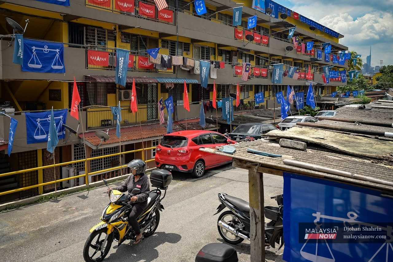 A motorcyclist passes a low-cost housing block hung about with party flags. A number of coalitions are vying for the support of voters although analysts say none of them might win enough to form the government on its own.