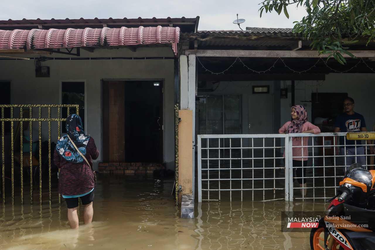 Di Taman Binjai Jaya, dua orang mangsa banjir berbual di pintu pagar sambil berdiri dalam air banjir setinggi buku lali.