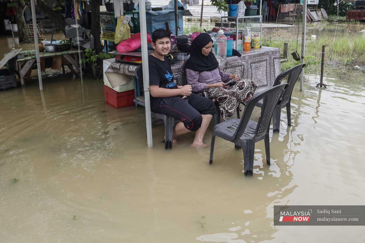 He and his mother sit at the small stall outside their house as they wait for the water level to recede. 