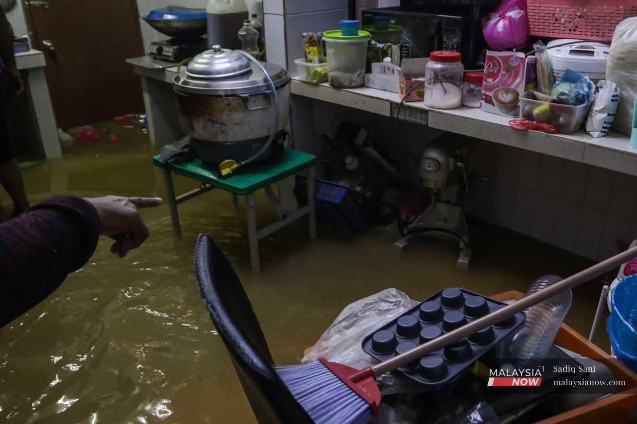 A resident points to her kitchen implements, some of which were moved to higher levels. Others, however, have likely sustained damage from the floodwater. 