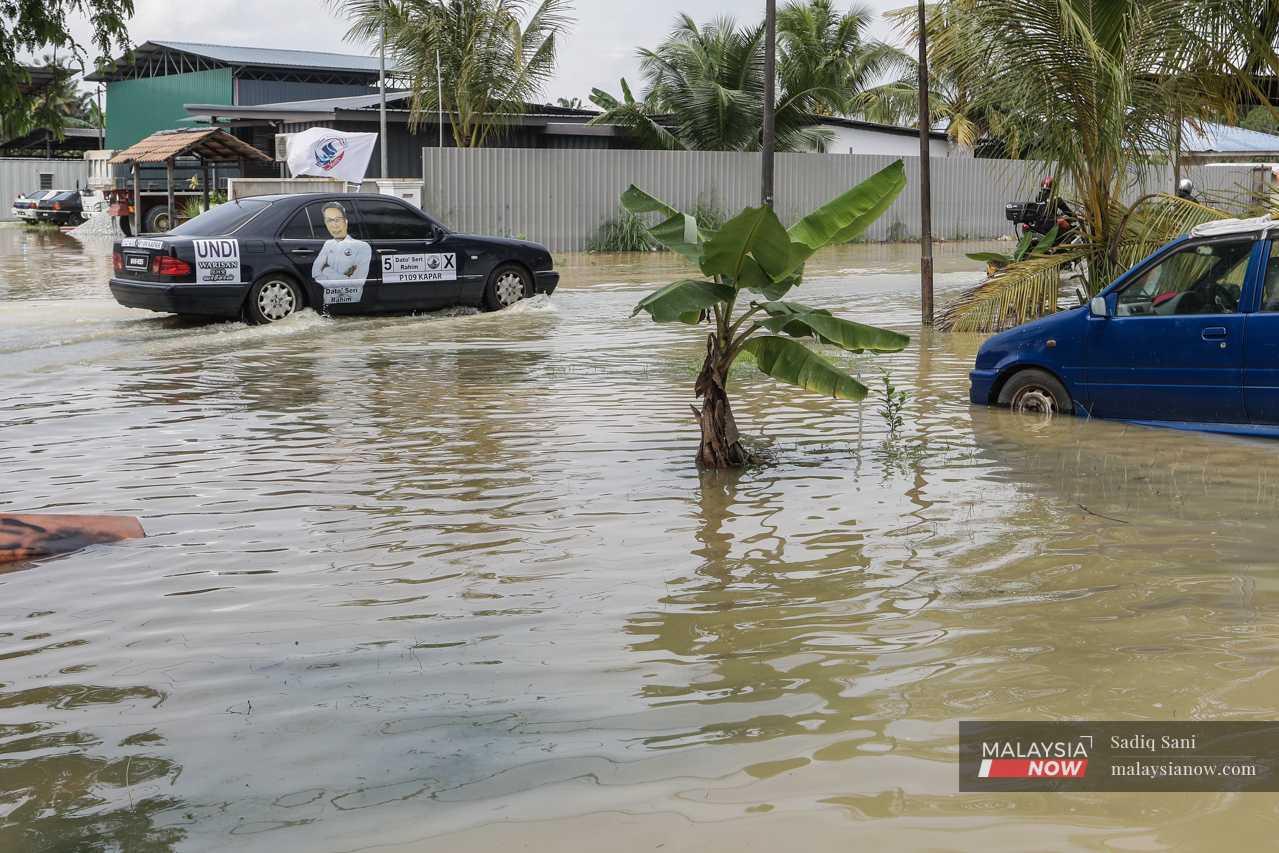 A car bearing an image of Warisan's candidate for the seat of Kapar passes through a flooded area in Jalan Paip. 
