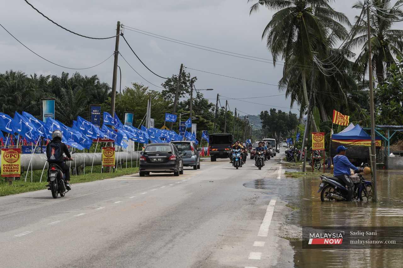 Seorang penunggang motorsikal (kanan) meredah air banjir di Jalan Paip, Meru, di mana bendera Barisan Nasional dinaikkan sempena pilihan raya.