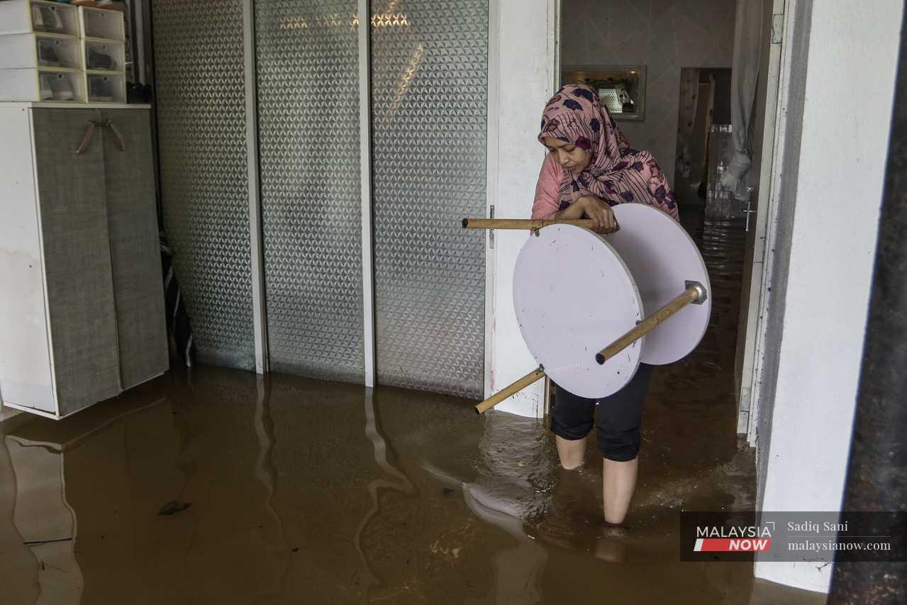 A woman carries a table out of her house in an attempt to save at least some furniture from flood damage. 

