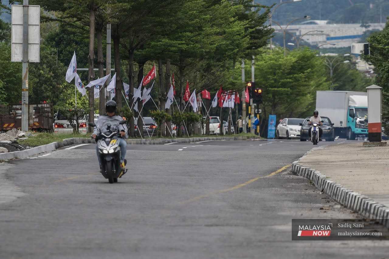 A motorcyclist passes the party flags of Pakatan Harapan and Warisan, put up at a road in Pandan ahead of the general election. 
