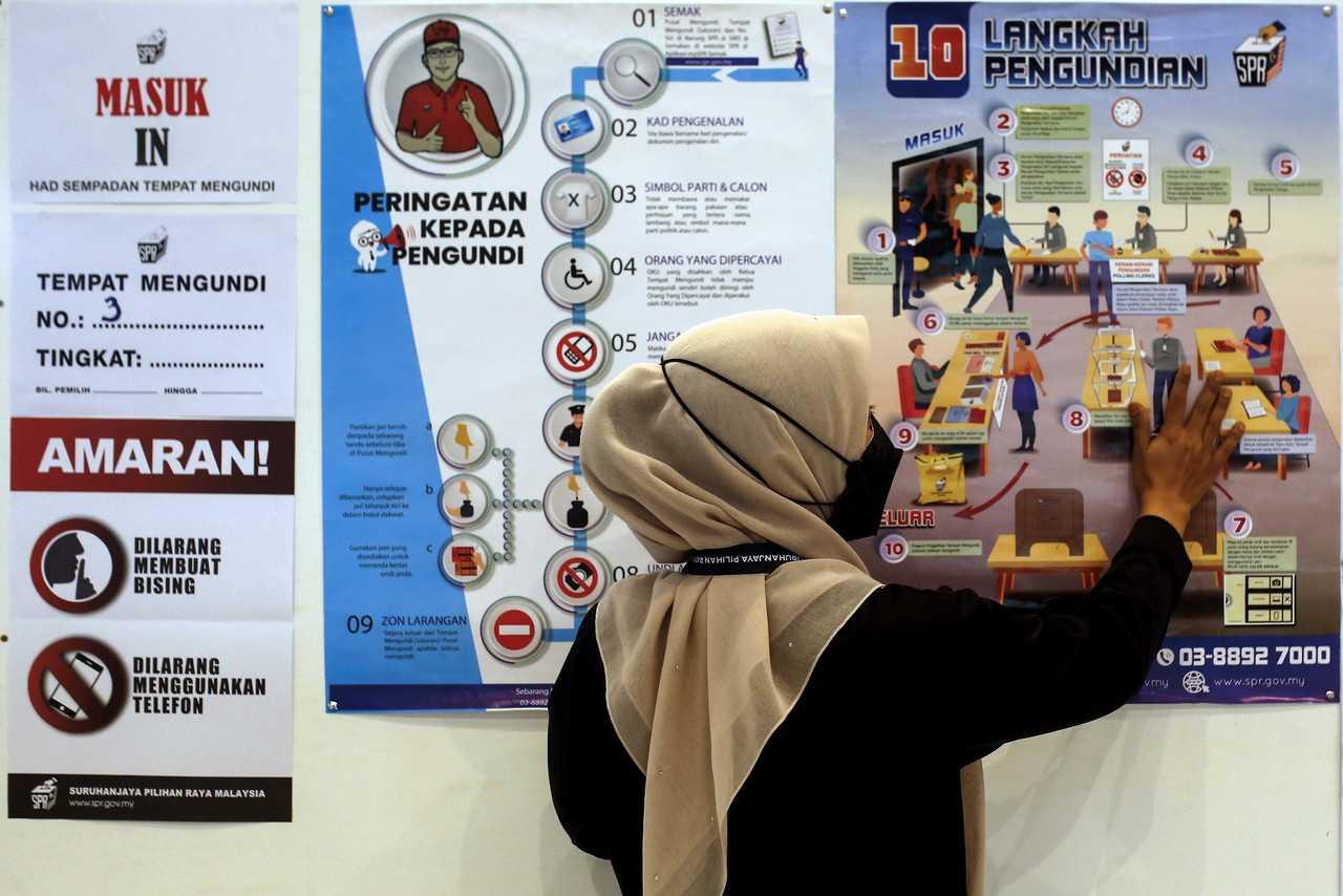 An Election Commission worker puts up a poster detailing the voting process at a voting centre in Port Dickson today. Photo: Bernama
