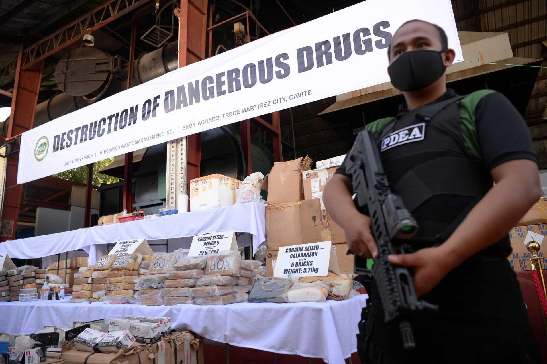 An armed agent of the Philippine Drug Enforcement Agency stands guard next to seized illegal drugs including bricks of cocaine prior to destroying them at a waste facility in Trece Martires, Cavite province on July 4, 2019. Photo: AFP 