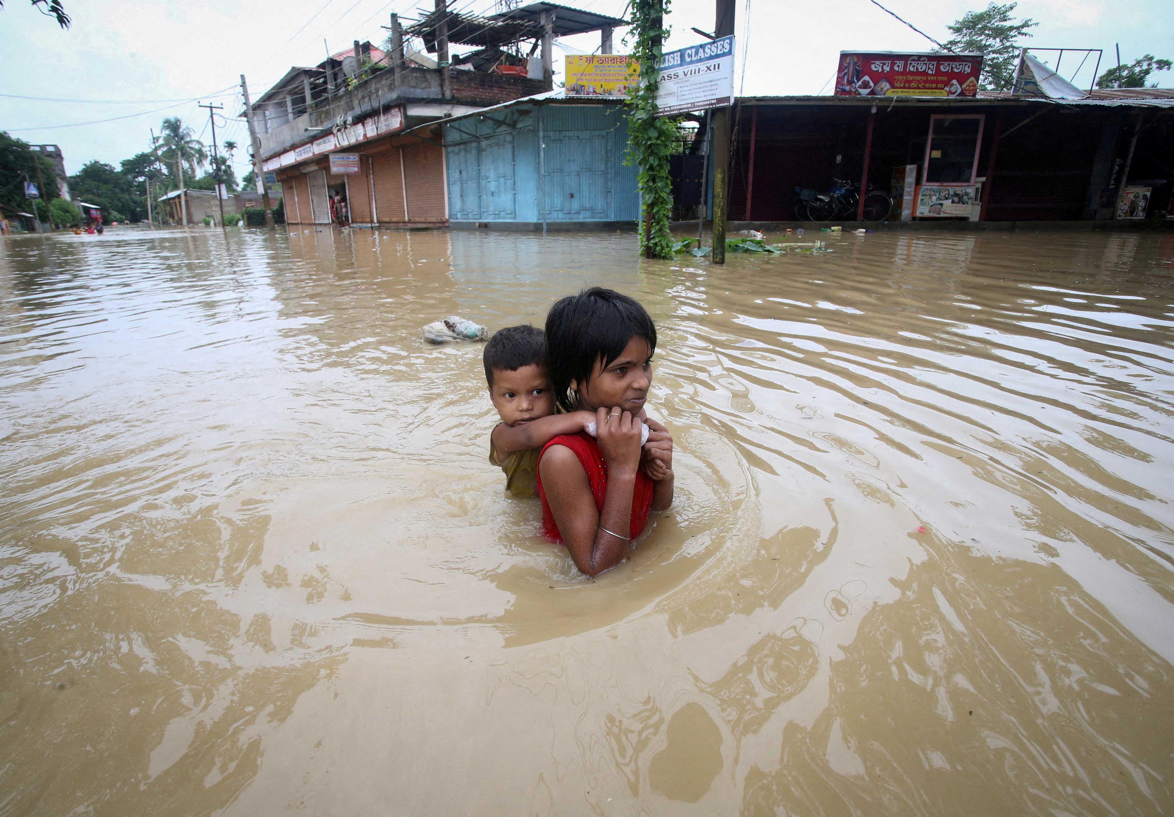 A girl carries her brother as she wades through a flooded road after heavy rains, on the outskirts of Agartala, India, June 18. Photo: Reuters