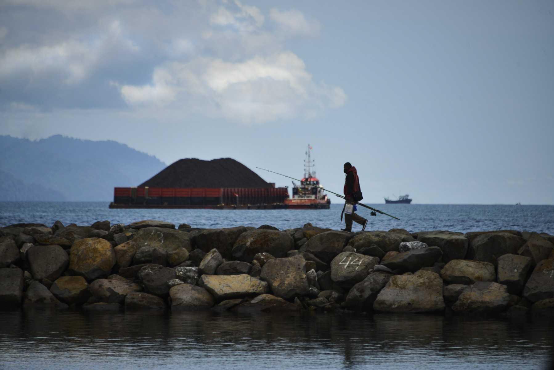 A man leaves after fishing as a tugboat pulling a barge filled with coal is seen along the coast of Banda Aceh on April 26, 2020. Photo: AFP